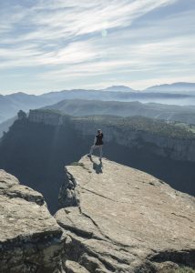 A person stepping outside of their comfort zone and standing on top of a steep cliff looking out at the horizon