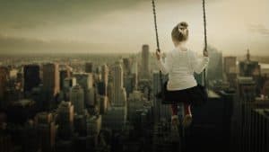 A little girl swinging on a swing overlooking a big city 