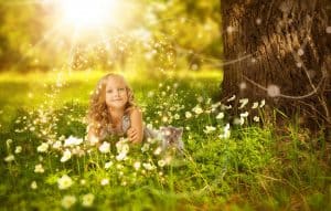 A little girl lying in the grass of a wooded area with a sunbeam and sparkles over her head to represent dreams
