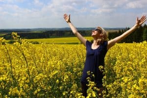 Happy person standing in a field of flowers with their arms raised in worship
