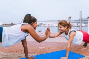 Two women doing a workout together on exercise mats and high fiving while holding a plank