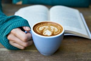 Closeup of a hand holding a latte that is sitting in front of a book