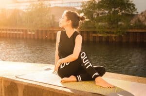 Woman wearing black fitness clothing performs yoga next to a river