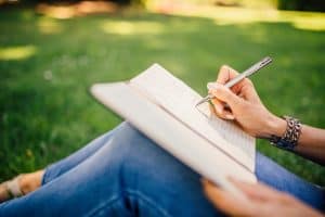 Closeup of a woman sitting outside in grass journaling in a notebook while wearing jeans
