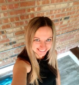 woman smiling with long blond hair looking up in front of a brick wall