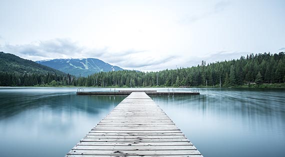A dock going into the pure blue water overlooking mountains.