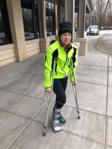 A woman with a broken ankle dressed in winter clothing wearing a cast on her right foot and holding crutches