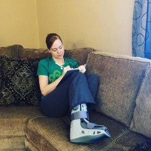 A woman journaling on the couch while wearing a cast on her right foot and ankle
