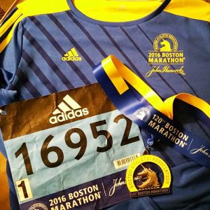 A Boston marathon jersey, medal, and bib number sitting flat on a table