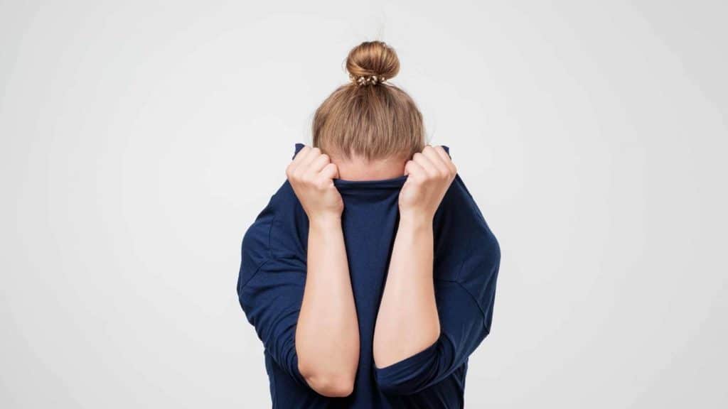 woman wearing a blue sweater with her hands lifting the sweater over her eyes in failure