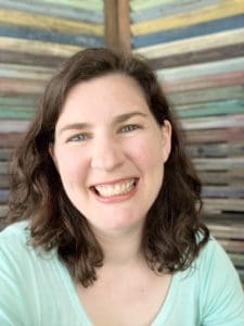 Woman with medium dark-brown hair wearing a sea-foam green shirt smiling. In the background is a colorful striped wall.