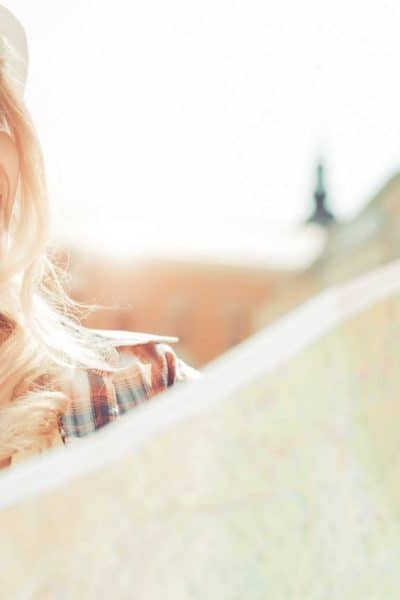 woman with long blonde hair wearing a hat looking at a map and staring off into the distance