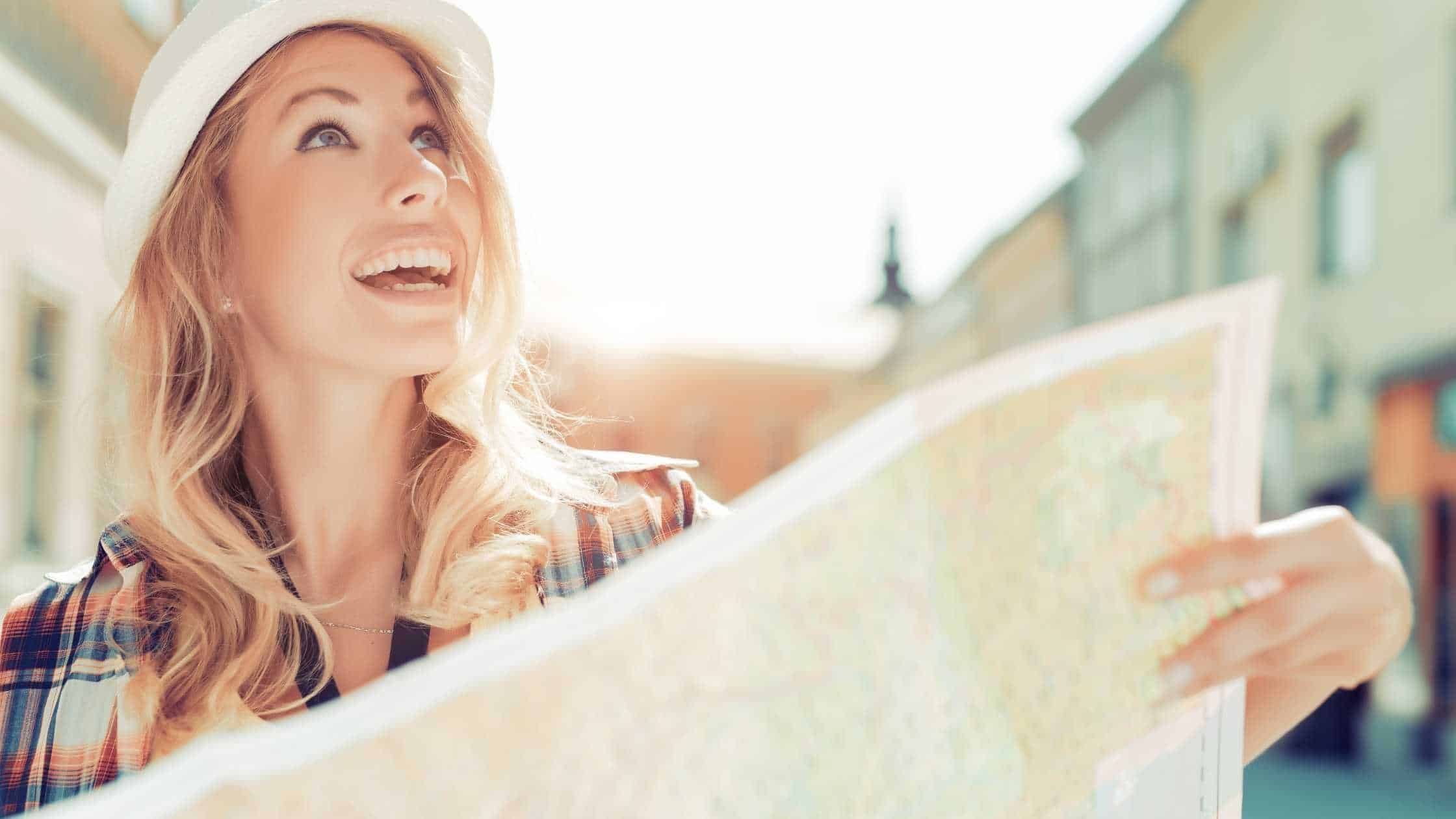 woman with long blonde hair wearing a hat looking at a map and staring off into the distance