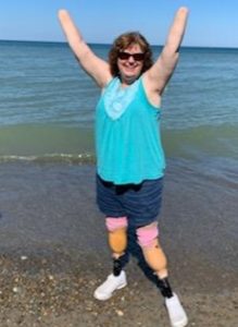 Quadruple amputee woman standing near the water lifting her arms in the air and smiling