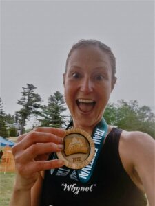 Woman with her mouth open in surprise holding up a medal from her 50-mile race