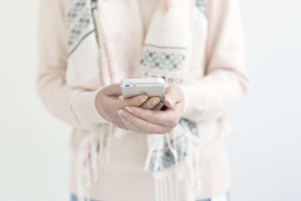 woman wearing a peach sweater and white scarf holding a smart phone