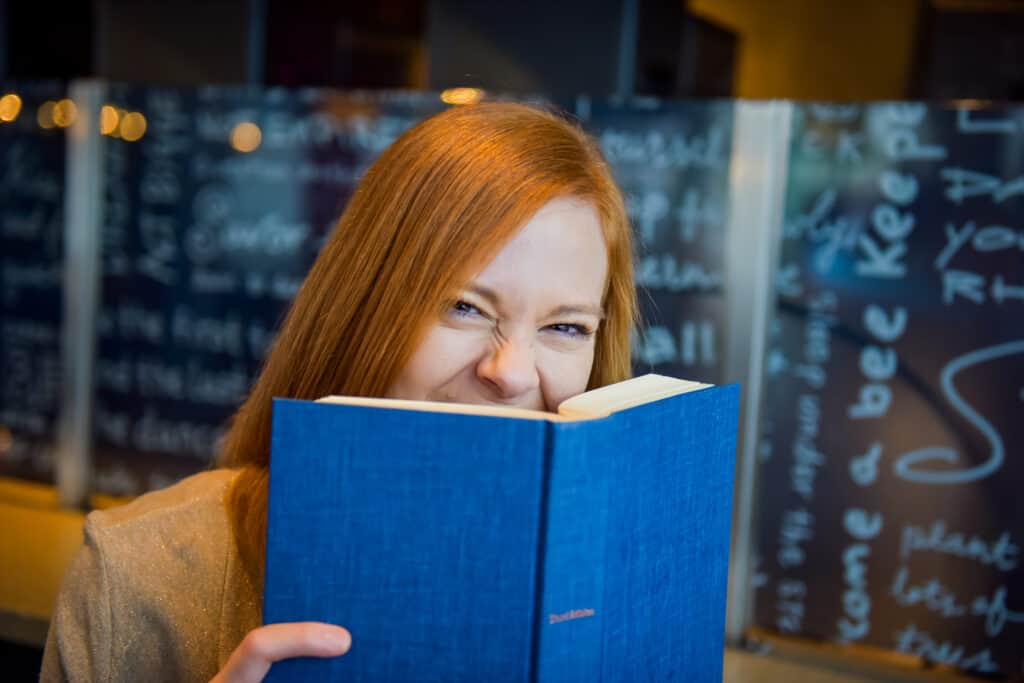 Gabe Cox with medium red hair at a coffee shop with her nose in a book