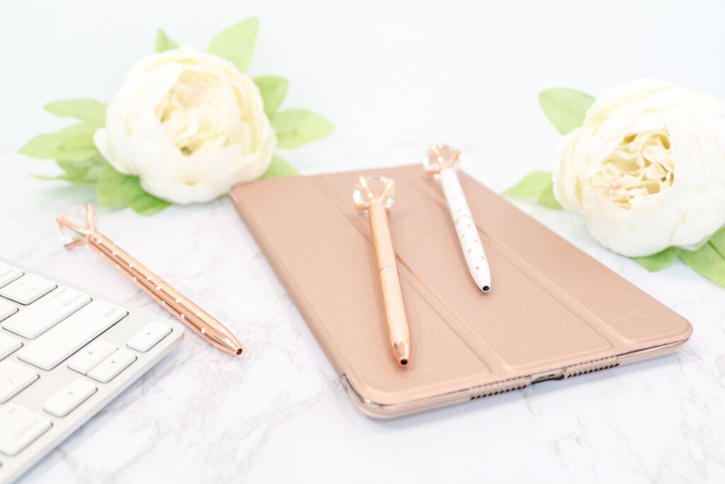rose gold journal with a rose gold pen and white pen on top and a white rose next to it