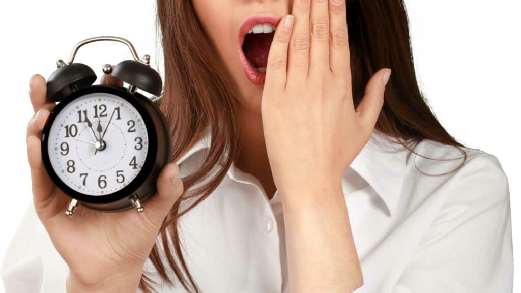 woman with mouth wide open and hand half covering it holding a small clock in her opposite hand