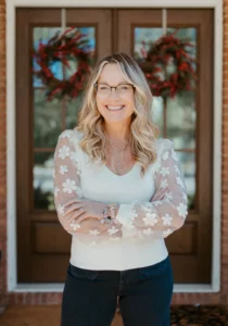 Headshot of Sandy Cooper standing in front of her front door wearing a white blouse and smiling